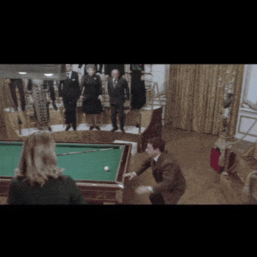 a group of people standing around a pool table with a man playing pool