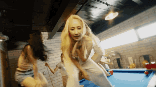 a group of women are dancing around a pool table in a room