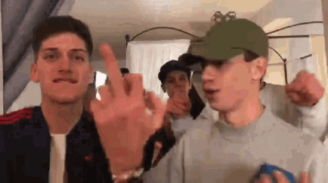 a group of young men are standing next to each other in a room and one of them is giving the middle finger .