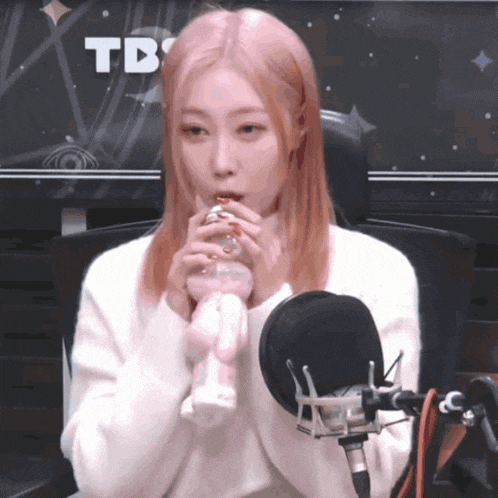 a girl with pink hair is sitting in front of a microphone with the word td on the screen behind her