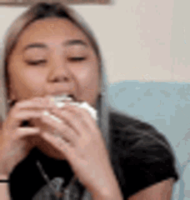 a woman is eating a sandwich with her eyes closed while sitting on a couch .