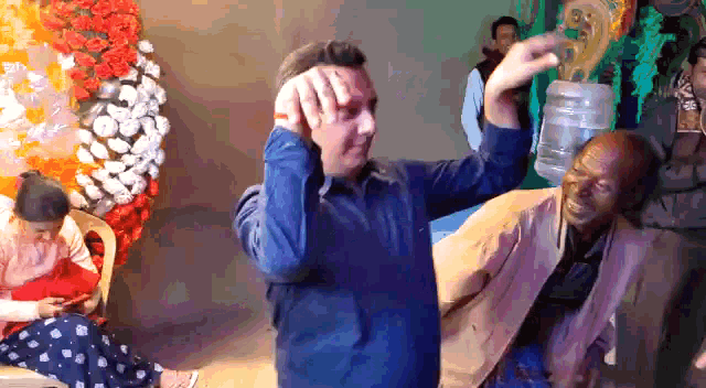 a man in a blue shirt is holding a bottle of water over his head