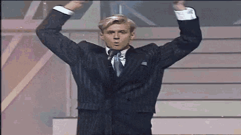a man in a suit is standing on a stage with his arms in the air .