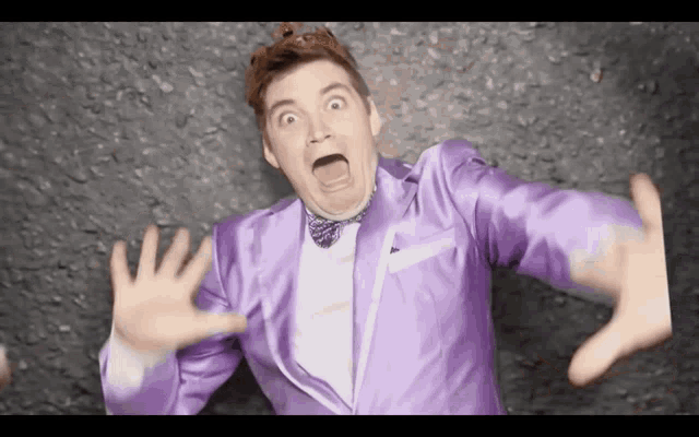 a man in a purple suit and bow tie makes a funny face