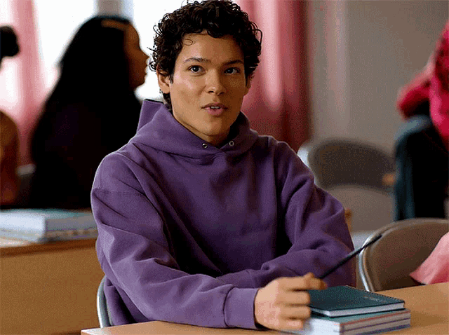 a boy in a purple hoodie sits at a desk