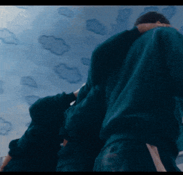 a man in a green sweatshirt is standing in front of a ceiling with clouds painted on it