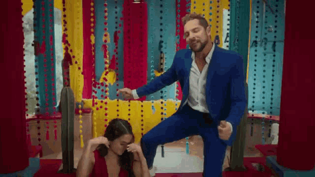 a man in a blue suit is dancing with a woman in a red dress in a colorful room .