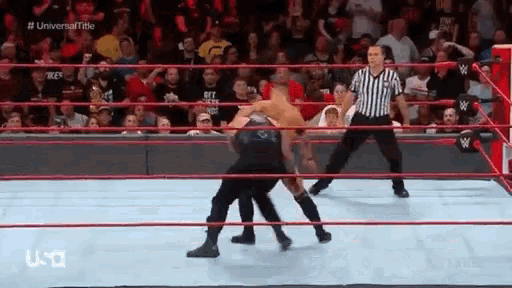 a referee is standing in the middle of a wrestling ring watching two men wrestling .