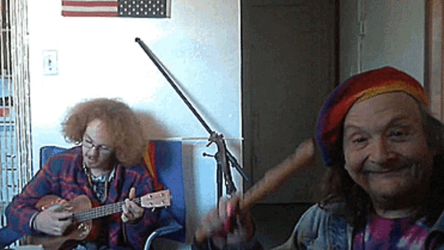 a man with curly hair is playing a guitar next to a woman in a rainbow hat