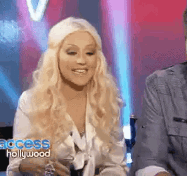 a woman with blonde hair is smiling while sitting next to a man on a television show .