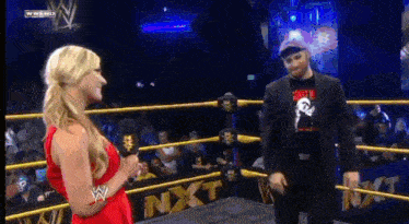 a woman in a red dress is talking to a man in a suit in a wrestling ring that has the word nxt on it