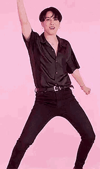 a young man in a black shirt and black pants is standing on one leg with his arms in the air .