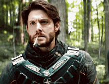 a man with a beard is smoking a cigarette in the woods .