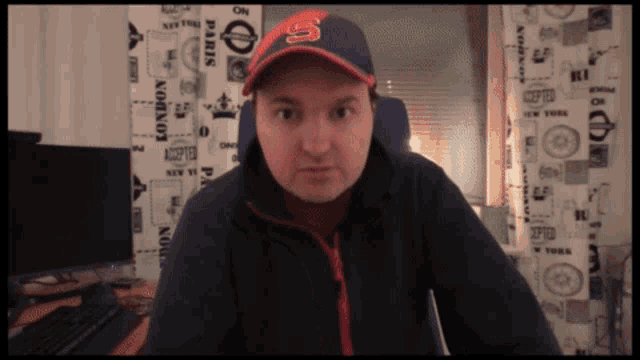 a man wearing a hat with the letter s on it looks at the camera