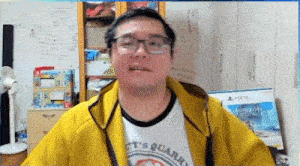 a man wearing glasses and a yellow jacket is talking on a video call in a room .