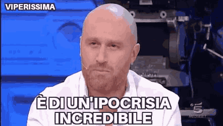 a bald man with a beard is sitting in front of a microphone and says edi un ipocrisisia incredibile .