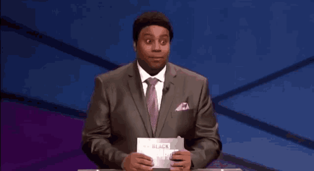 a man in a suit and tie is holding a piece of paper that says be black
