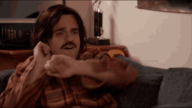 a man with long hair and a mustache is sitting on a couch with his feet up