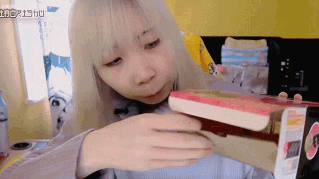a girl with white hair is opening a box with chinese writing on the bottom