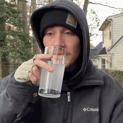 a man wearing a columbia jacket is drinking from a glass