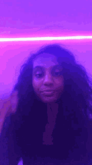 a woman is standing in front of a purple wall with a purple light behind her .
