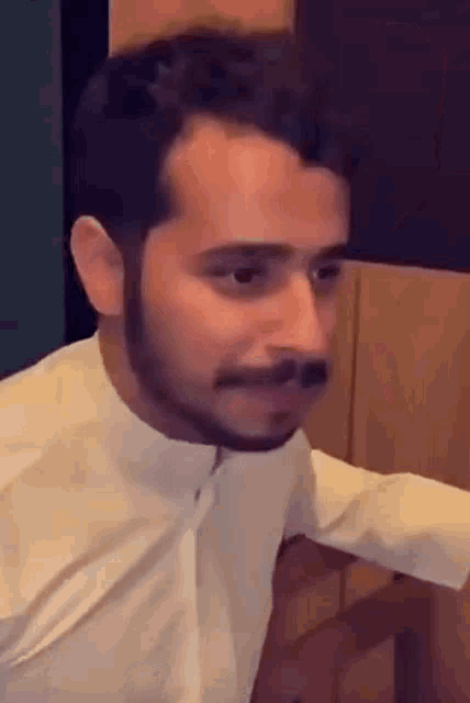 a man with a beard is wearing a white shirt and looking at the camera .