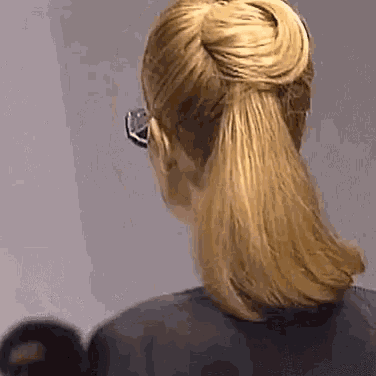 a woman wearing glasses and a ponytail is standing in front of a wall .
