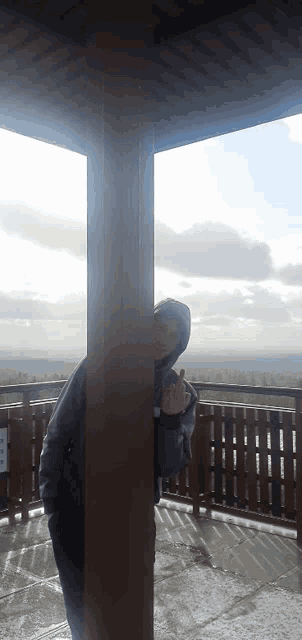 a man in a hooded jacket stands behind a wooden pole and gives the middle finger