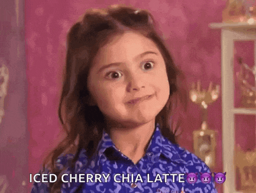 a little girl in a blue shirt is making a face and saying iced cherry chia latte .