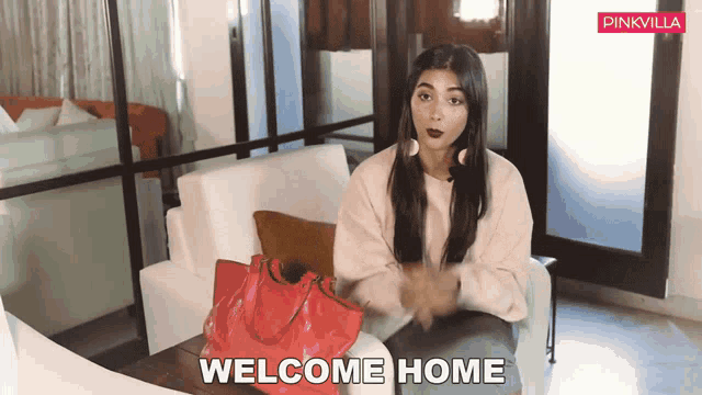 a woman is sitting on a couch with a red purse and the words welcome home behind her