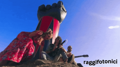 a group of people are sitting in front of a giant fist and the word raggifotonici is on the bottom right