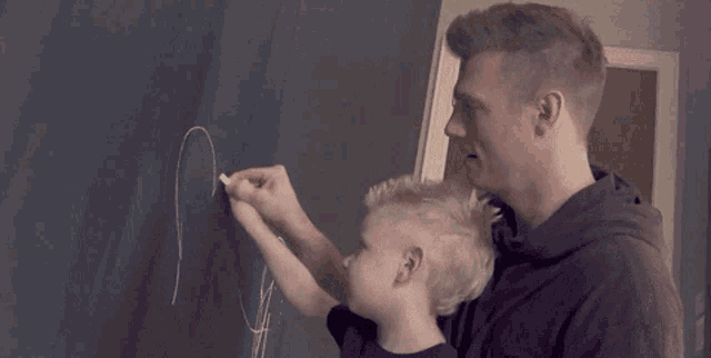 a man and a child are writing on a blackboard with chalk