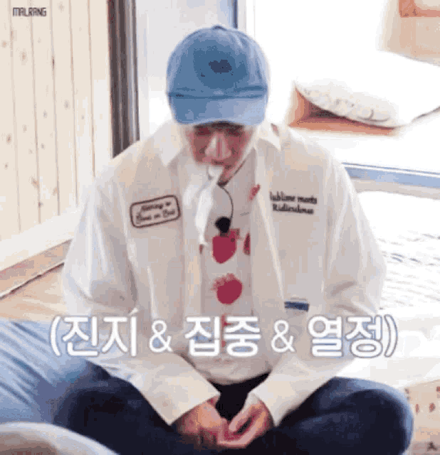 a man wearing a blue hat and a white shirt with a strawberry on it sits on the floor