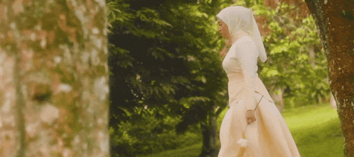 a woman in a white dress with a hijab is walking in a park