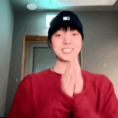 a young man wearing a red sweater and a black hat is clapping his hands together .