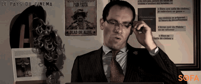 a man in a suit and tie is talking on a cell phone with a dead or alive sign behind him