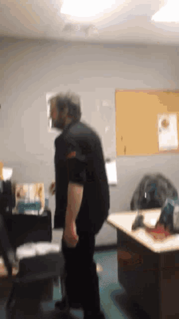a man in a black shirt is standing in a room with a desk