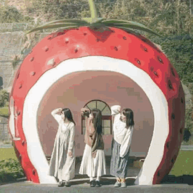 three women are posing for a picture in front of a strawberry bus stop