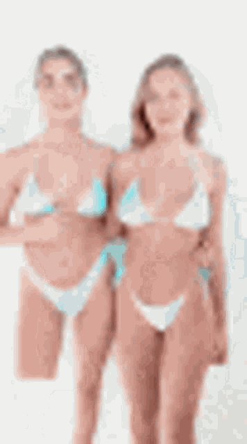 two women in bikinis are standing next to each other on a white surface .