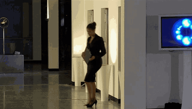 a woman in a black dress stands in a hallway next to a television