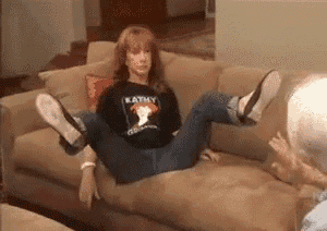 a woman is sitting on a couch with her legs crossed while wearing a katmy shirt .