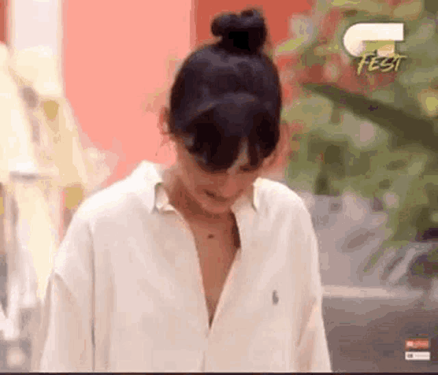 a woman is wearing a white shirt with a collar that is open and a bun in her hair .