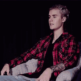 a young man wearing a plaid shirt is sitting in a chair