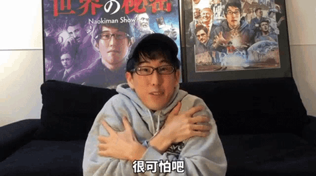 a man sitting on a couch with his hands on his chest in front of a naokiman shaw poster