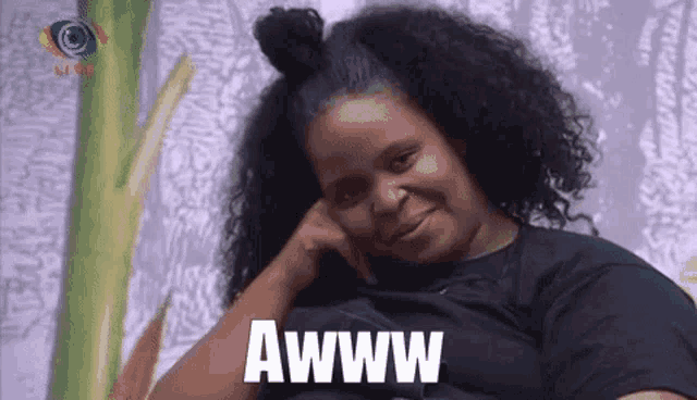 a woman with curly hair is sitting on a couch with her hand on her chin and the word awww written on the screen .
