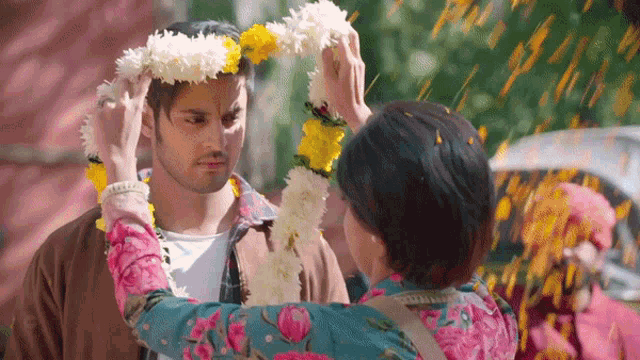 a woman is putting flowers on the head of a man