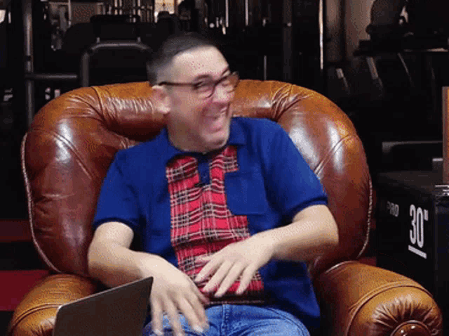 a man in a blue plaid shirt is sitting in a chair with a laptop on his lap