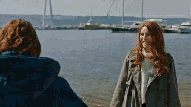 a woman with red hair is standing next to a body of water with boats in the background