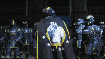 a group of soldiers are standing in a line with one wearing a black cape with a globe and stars on it
