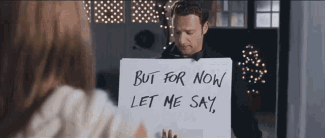 a man is holding a sign that says " but for now let me say "